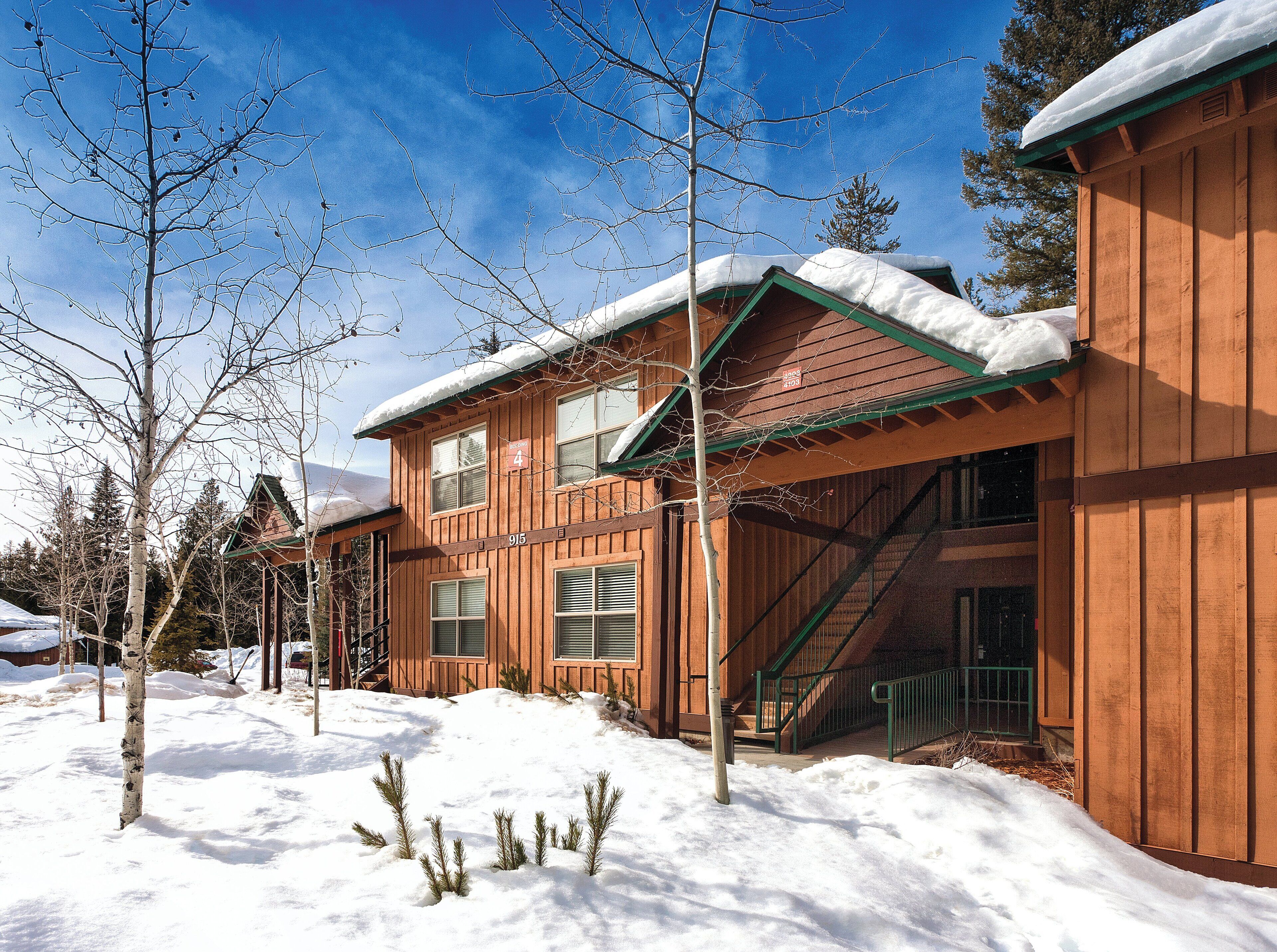 A wooden cabin with a green roof, a staircase, and a snow-covered ground.