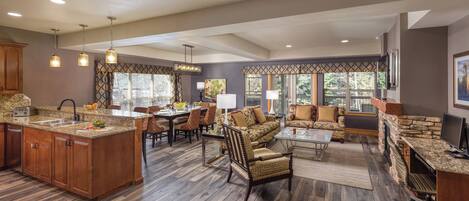 A spacious kitchen with granite countertops, a dining area with a large table and chairs, a living room with a sofa and armchairs, and a stone fireplace.