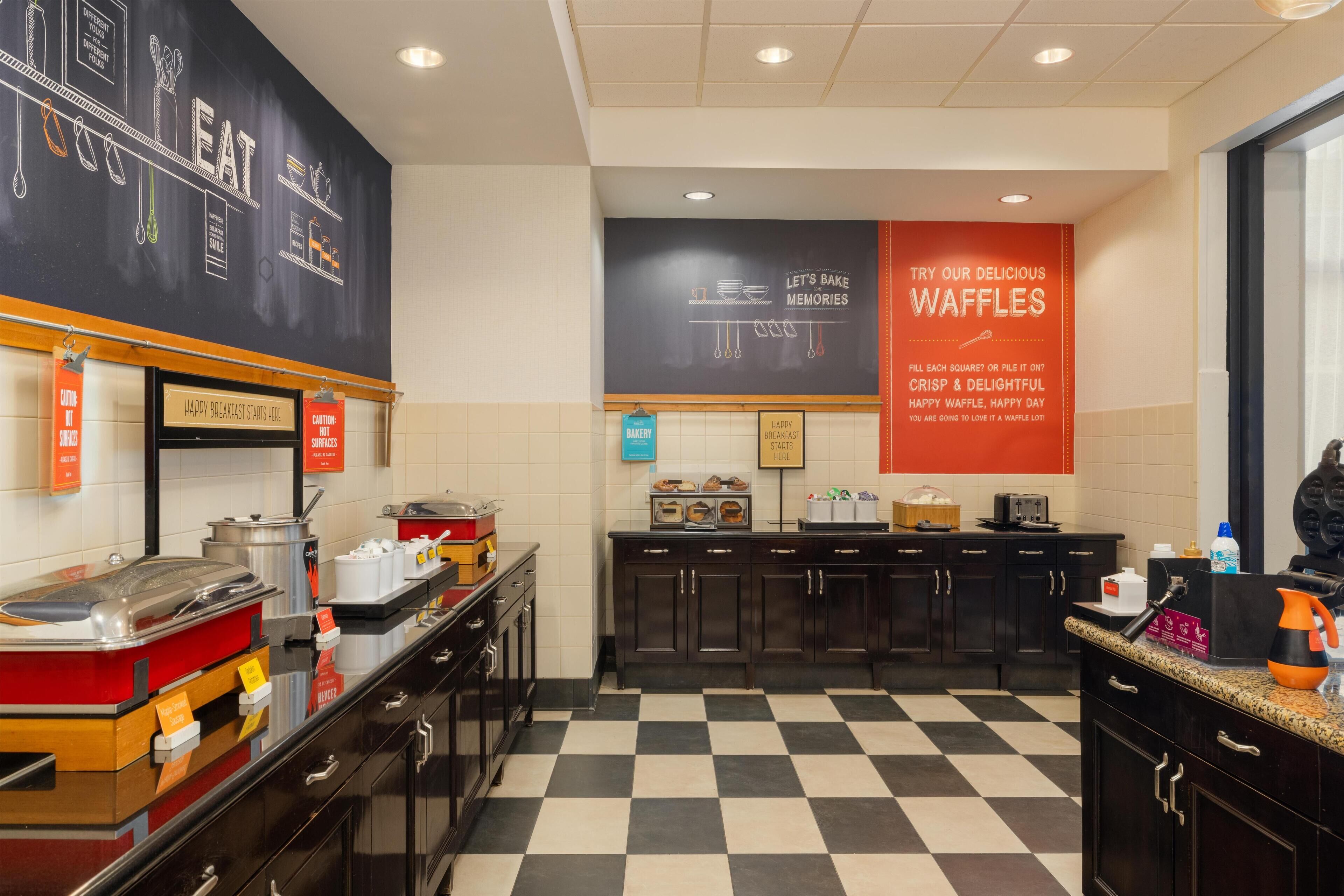 A breakfast area with a checkered floor, a chalkboard with food-related drawings, and a sign promoting waffles.