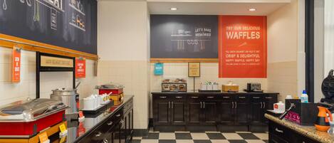 A breakfast area with a checkered floor, a chalkboard with food-related drawings, and a sign promoting waffles.