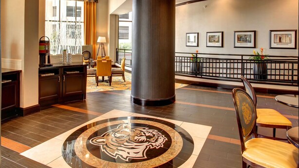 Un hall d’entrée avec une colonne centrale, un logo représentant un tigre sur le sol, un comptoir d’accueil et des tableaux encadrés au mur.