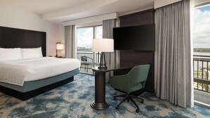 A hotel room with a bed, a desk with a chair, a TV, and a view of the outdoors.