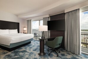 A hotel room with a bed, a desk with a chair, a TV, and a view of the outdoors.