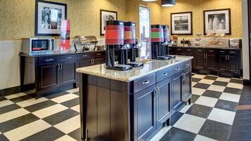 A kitchen with a checkered floor, a microwave, coffee makers, and framed pictures on the wall.