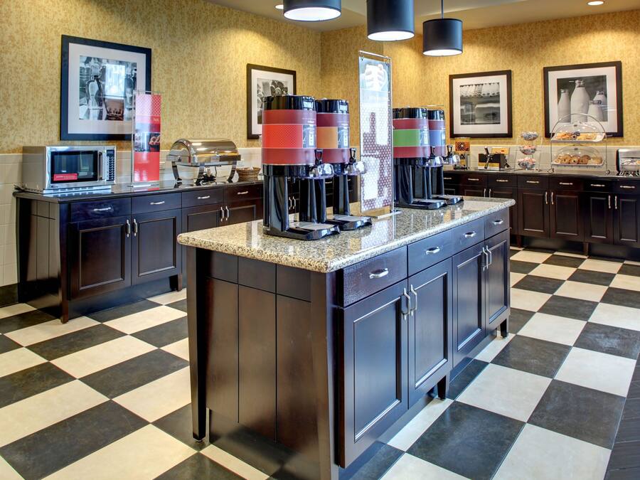 A kitchen with a checkered floor, a microwave, coffee makers, and framed pictures on the wall.
