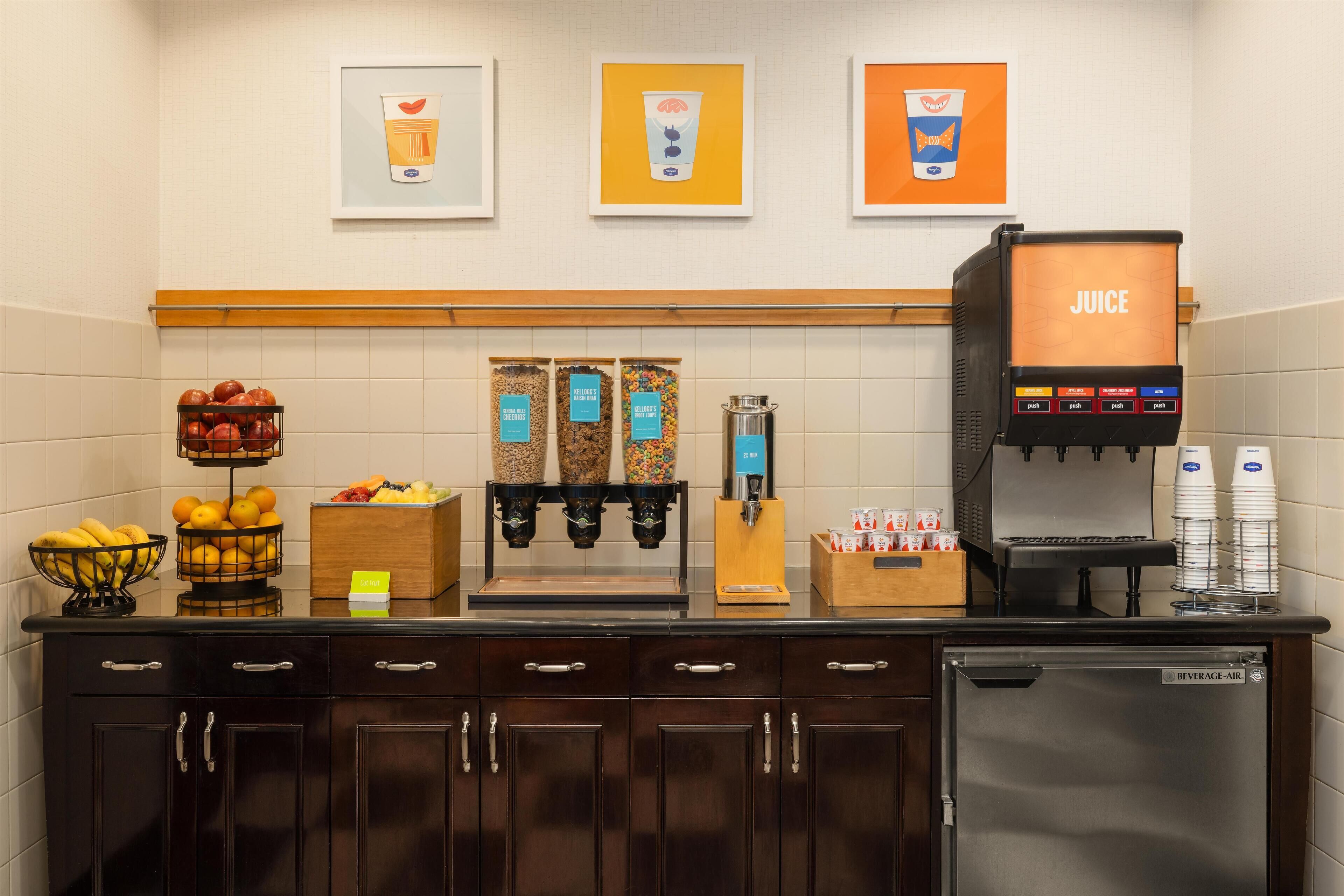 A kitchenette with a juice dispenser, fruit baskets, and a beverage machine.