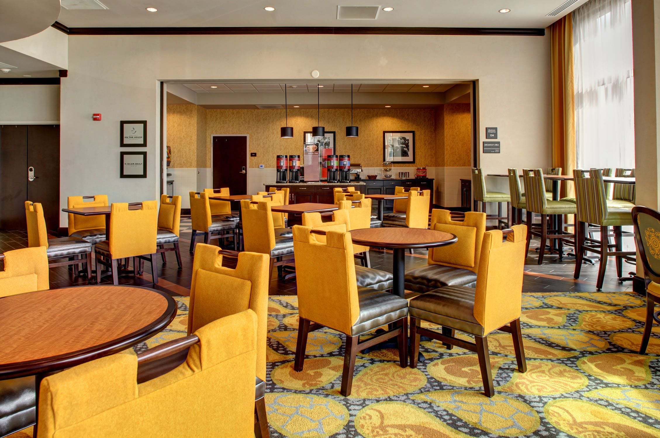 A hotel dining area with yellow chairs, round tables, and a coffee bar.