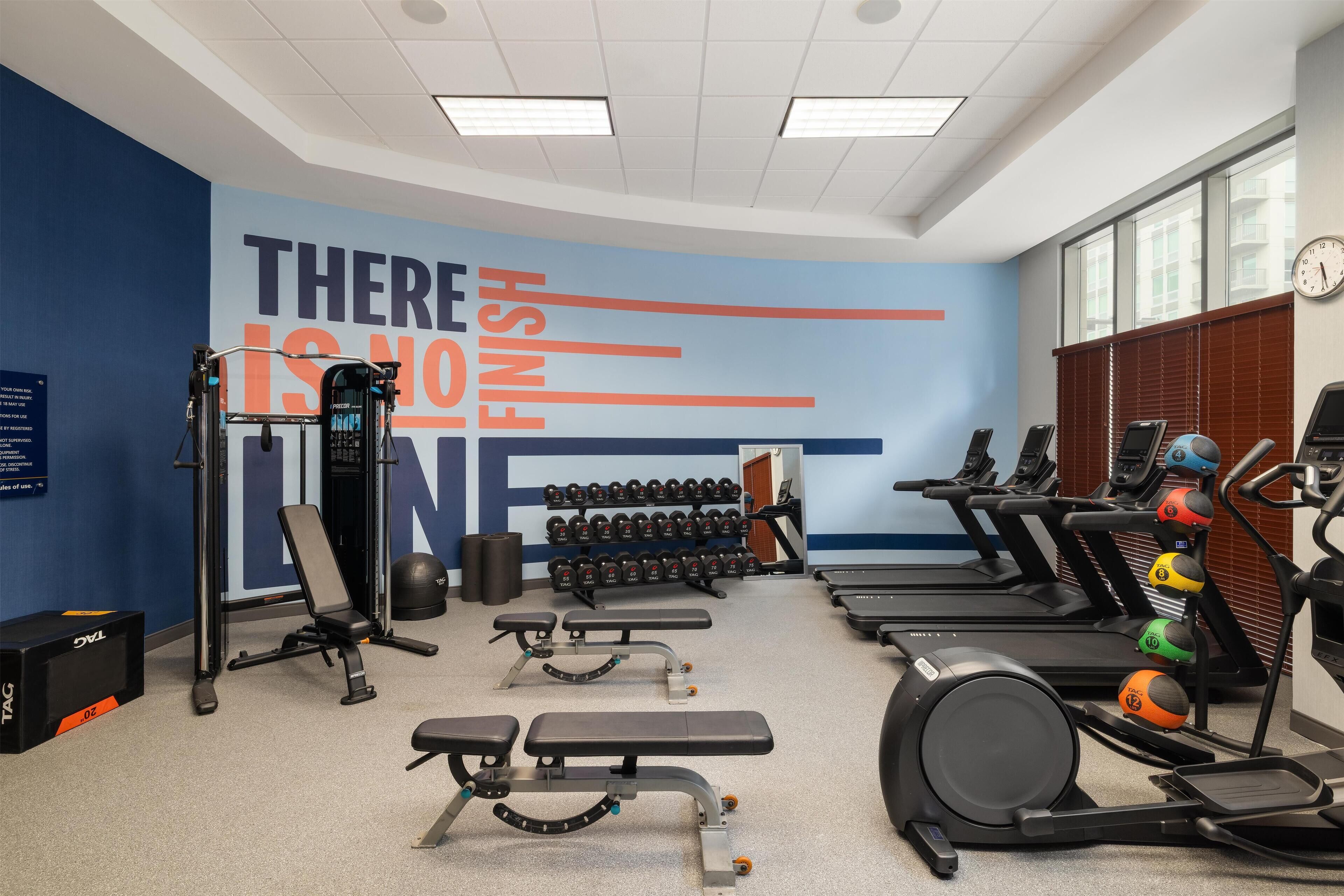 Une salle de sport équipée de tapis de course, de bancs de musculation, d’haltères et d’un mur d’inspiration.