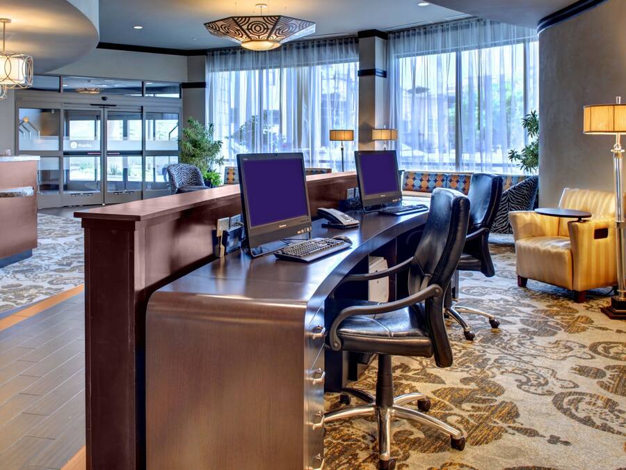 A hotel reception area with a reception desk, computers, seating, and large windows.
