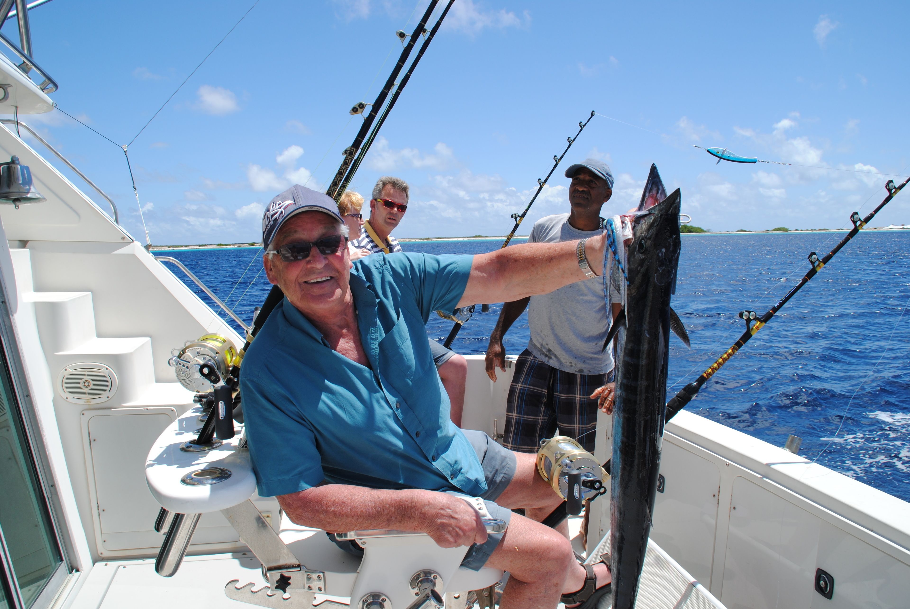 A boat with a person steering, another person holding a fishing rod, and a third person standing by.
