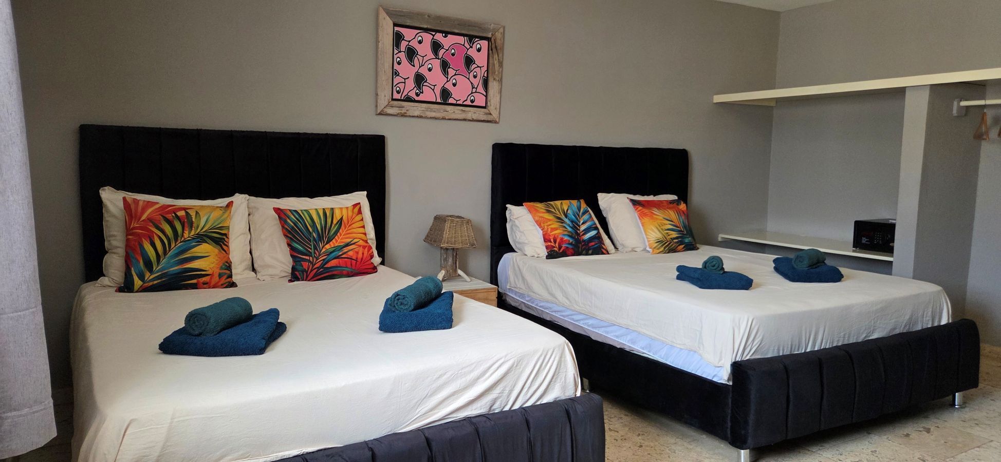 Dos camas dobles con ropa blanca, cabeceros negros y coloridas almohadas con motivos tropicales.