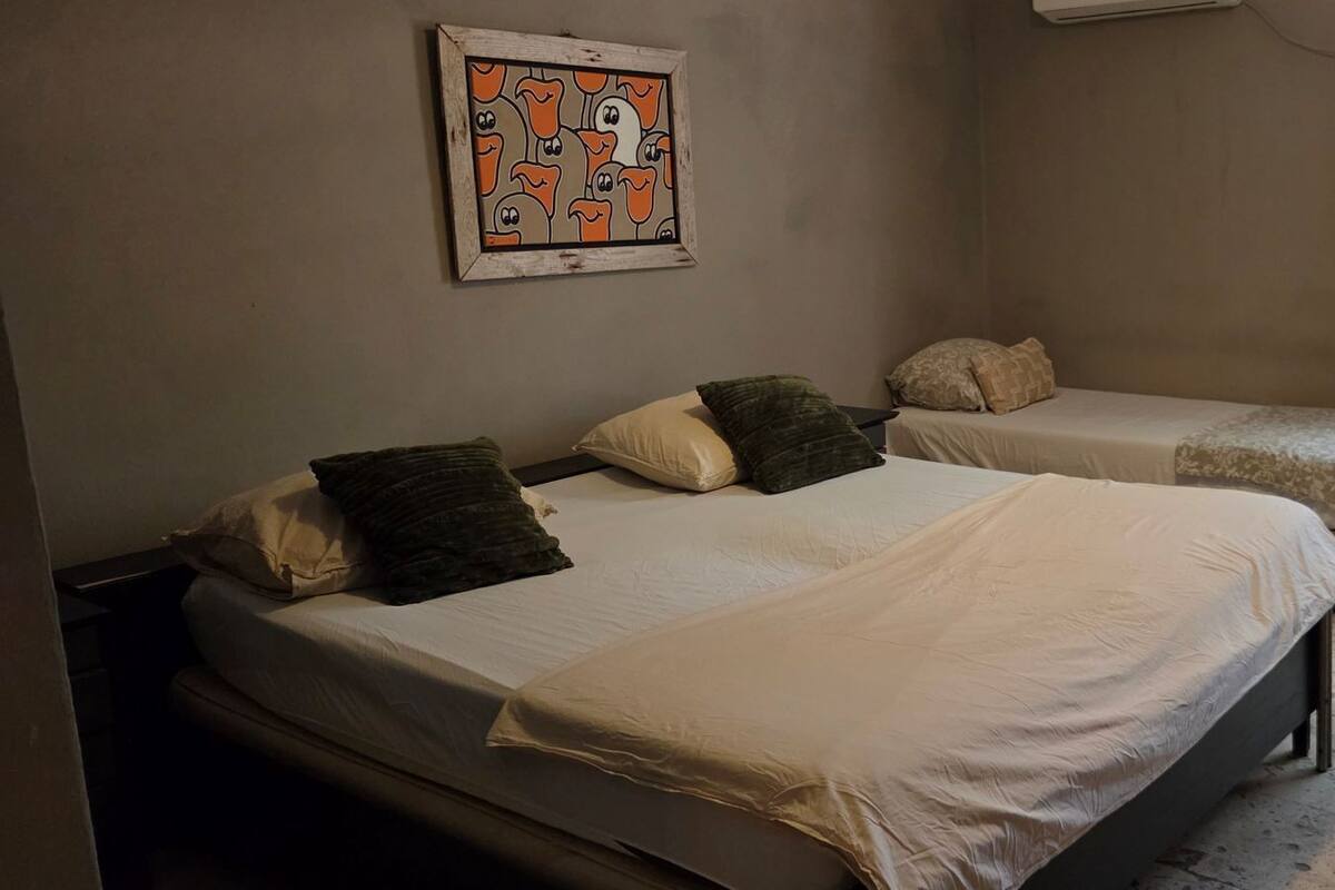 Une chambre avec deux lits, une œuvre d’art encadrée et une fenêtre avec des rideaux.