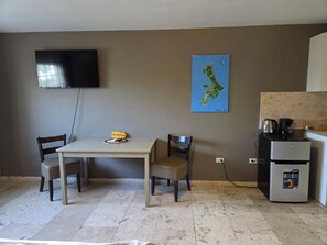 A room with a dining table, two chairs, a television mounted on the wall, a small refrigerator, and a map on the wall. - The Lodge Bonaire (Kralendijk)