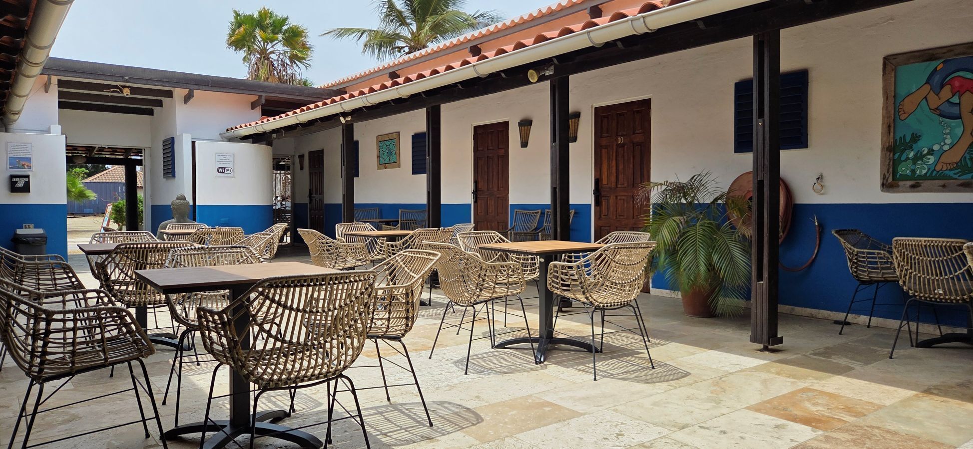 Un área de café al aire libre con mobiliario de mimbre y piso de baldosas.