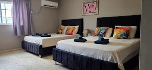 Dos camas individuales con cabeceras y pies de cama a juego, una ventana con cortinas, un equipo de aire acondicionado y una obra de arte colgada en la pared.