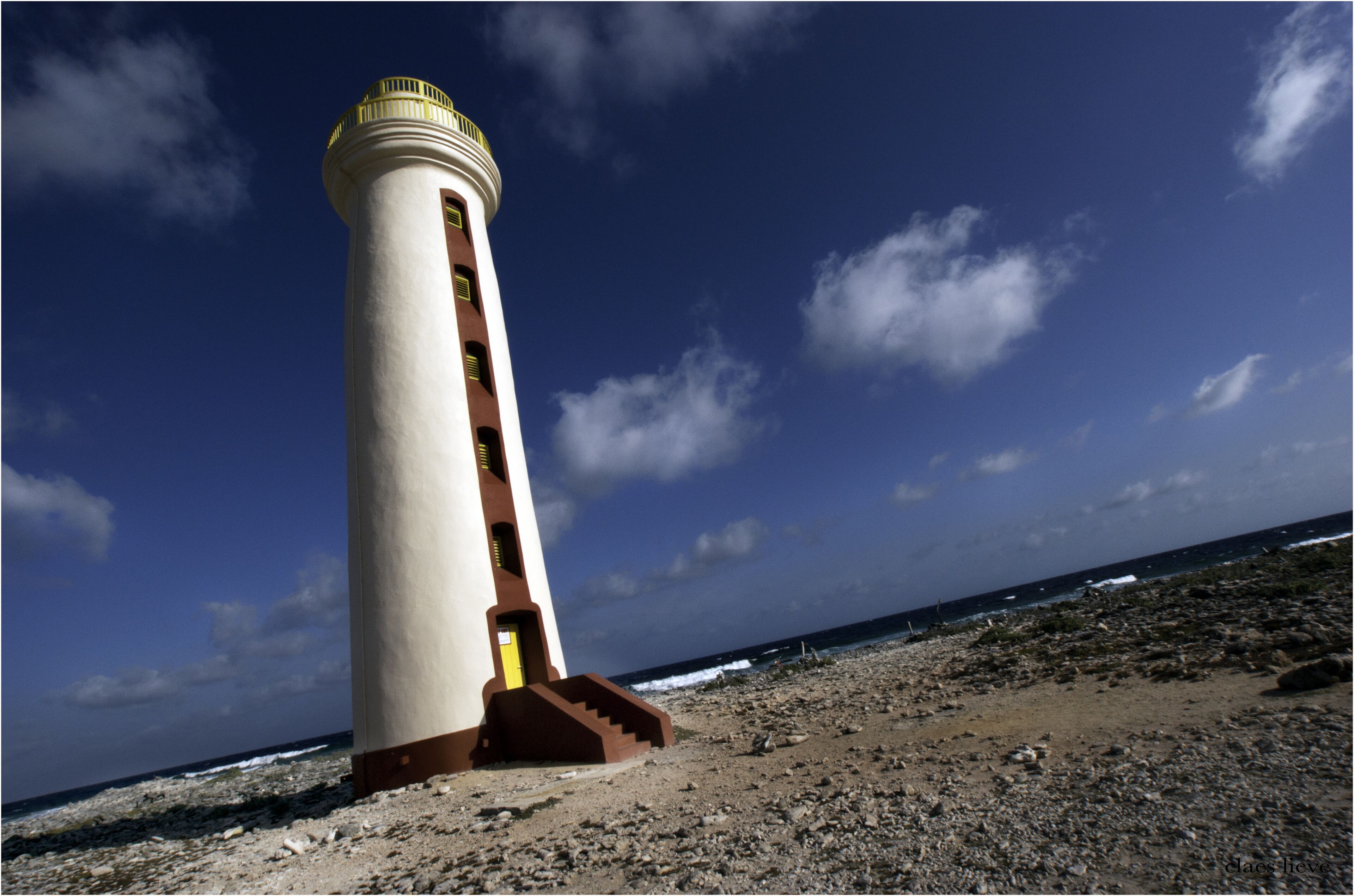 A lighthouse with a spiral staircase leading to the top, situated on a rocky beach with the ocean in the background.