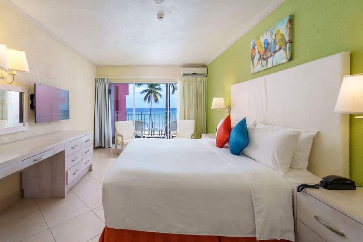 A hotel room with a bed, bedside table, desk, and a view of the ocean.