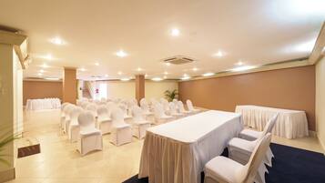 A conference room with rows of white chairs, a long table, and a staircase in the background.