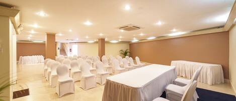 Un salón de conferencias con filas de sillas blancas, una mesa larga y una escalera al fondo.