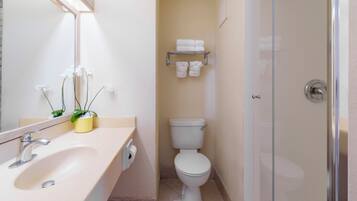 Casa de banho com lavatório, sanita e chuveiro. Inclui um espelho, porta-toalhas e uma planta em vaso.