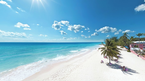 Een strand met wit zand, helder turquoise water en wuivende palmbomen.