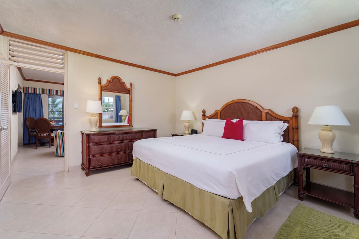 A hotel room with a large bed, wooden headboard, two bedside tables with lamps, a dresser, and a mirror.