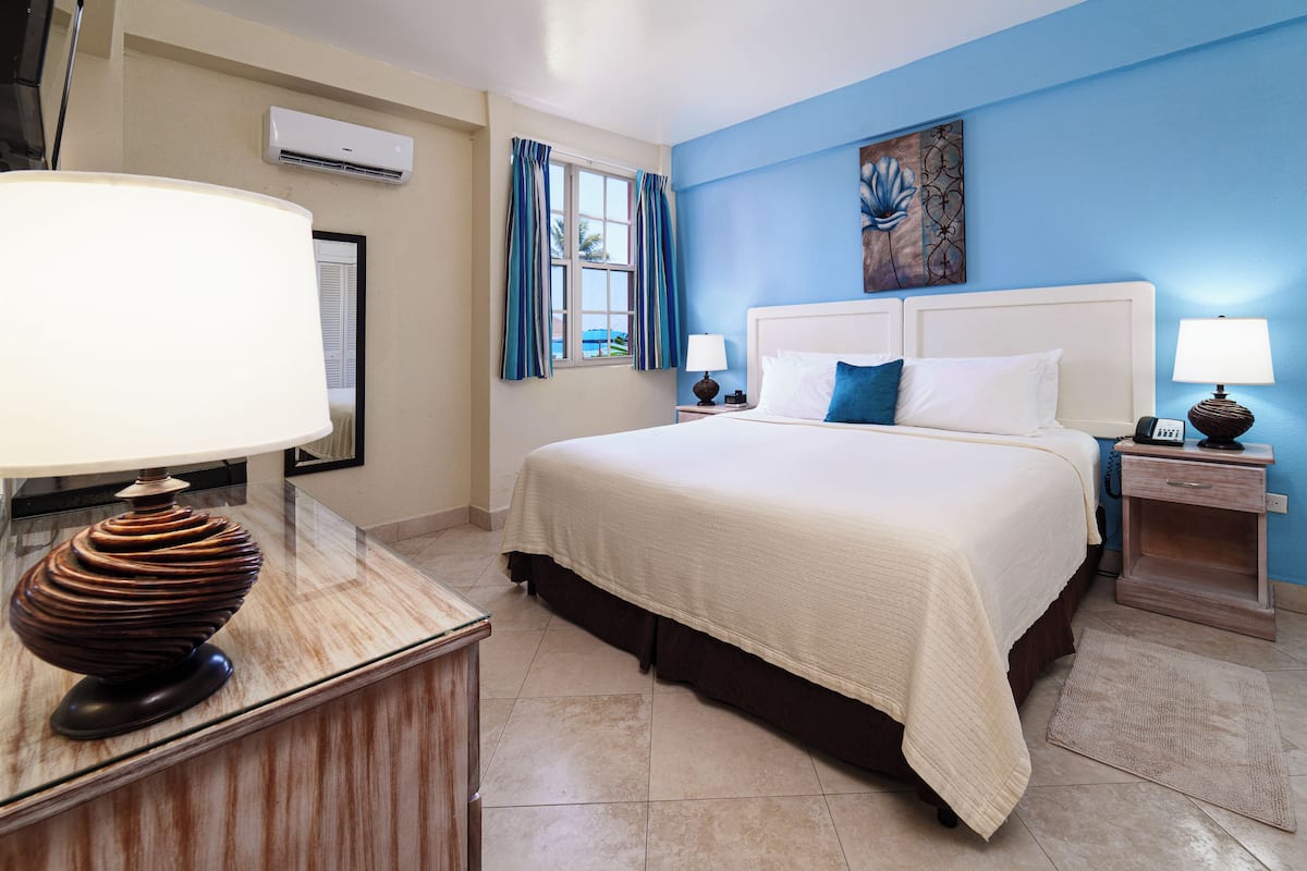 A hotel room with a large bed, two bedside tables with lamps, a wall-mounted air conditioner, and a window with curtains.