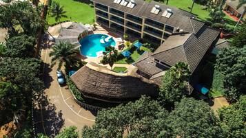 An aerial view of a hotel with a swimming pool, multiple balconies, and lush greenery.