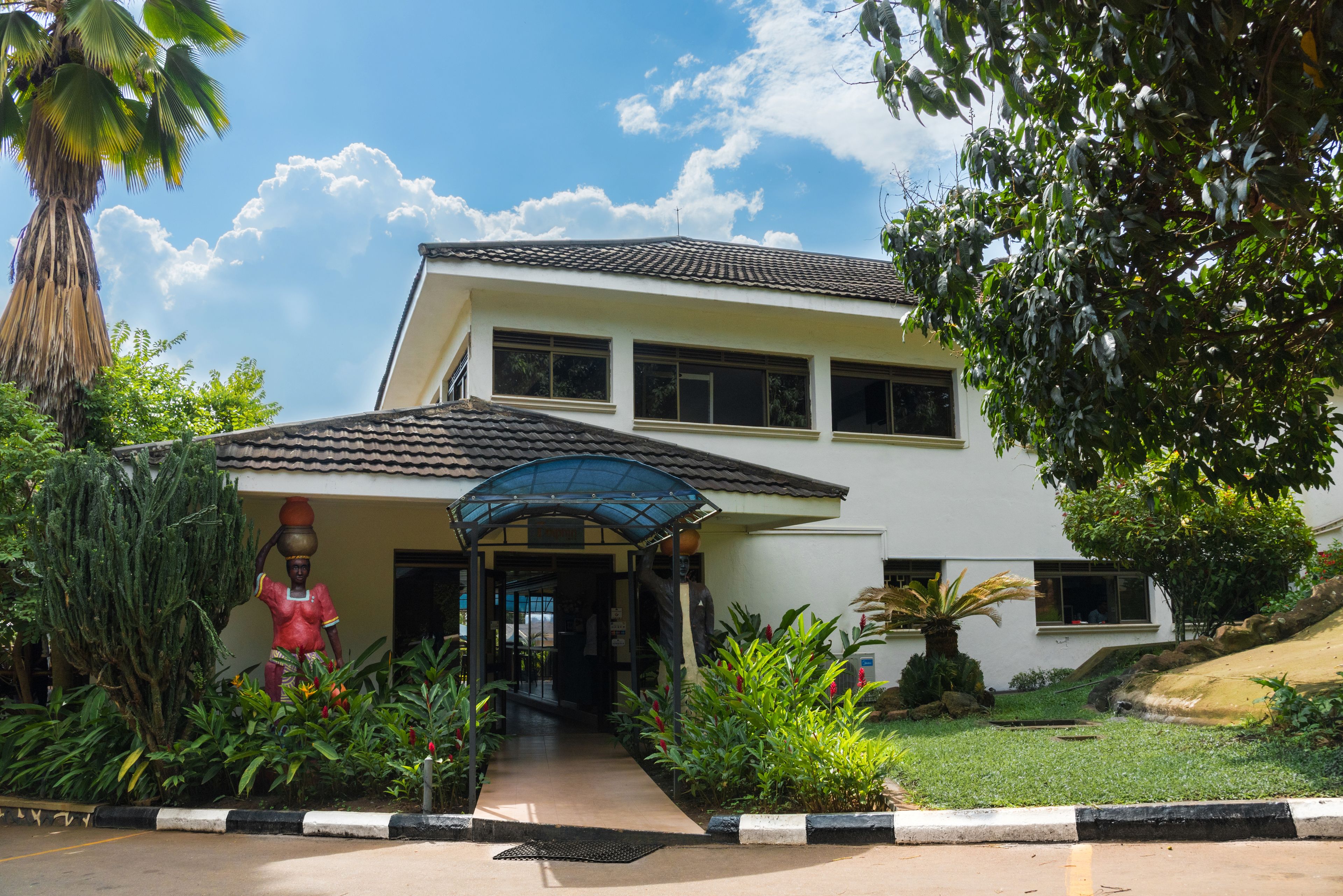 A two-story building with a tiled roof, a covered entrance, and a well-maintained garden with various plants and a palm tree.