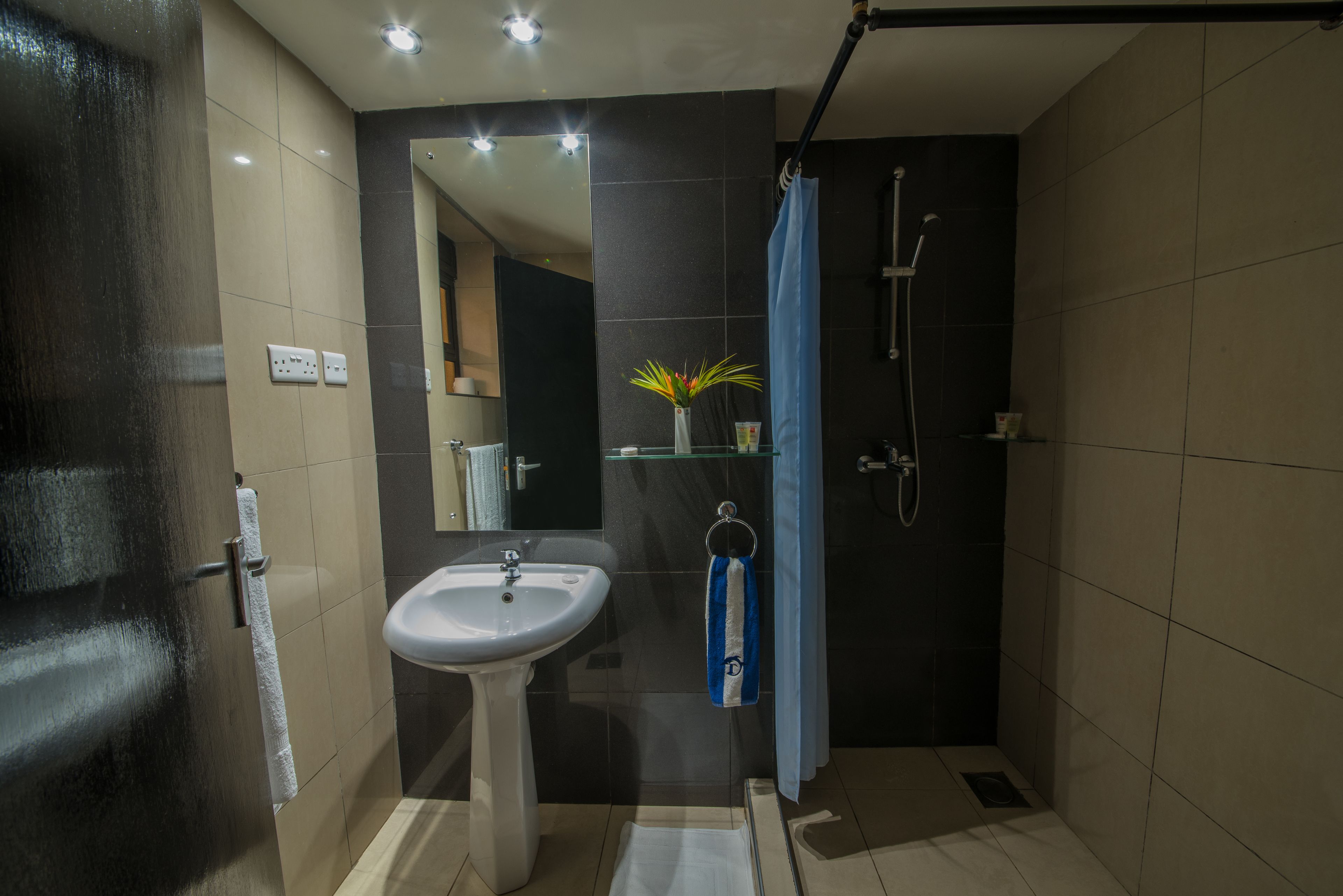 A modern bathroom with a white sink, a glass shower enclosure, and a blue shower curtain.
