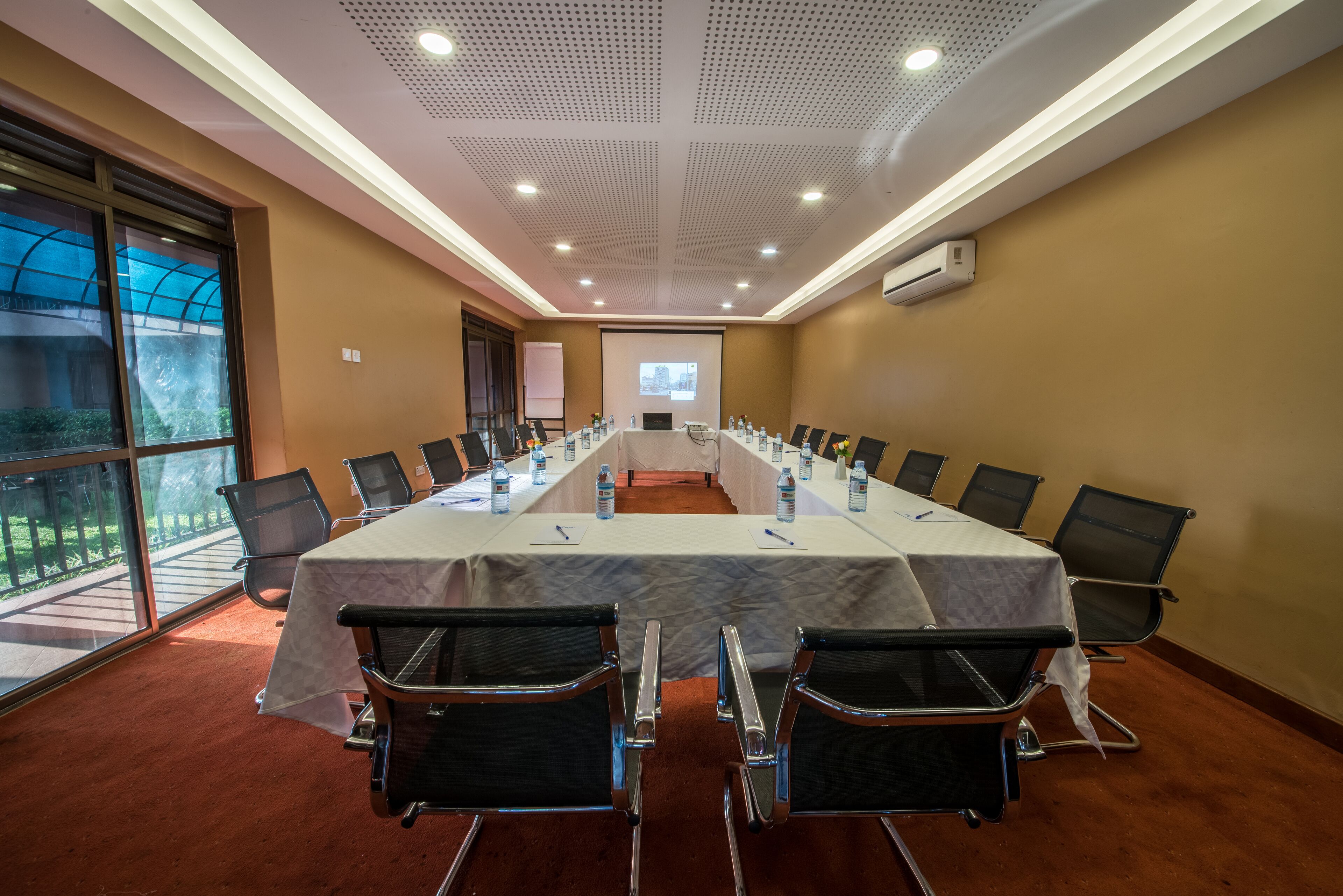 A conference room with a long table, chairs, a projector screen, and a large window.