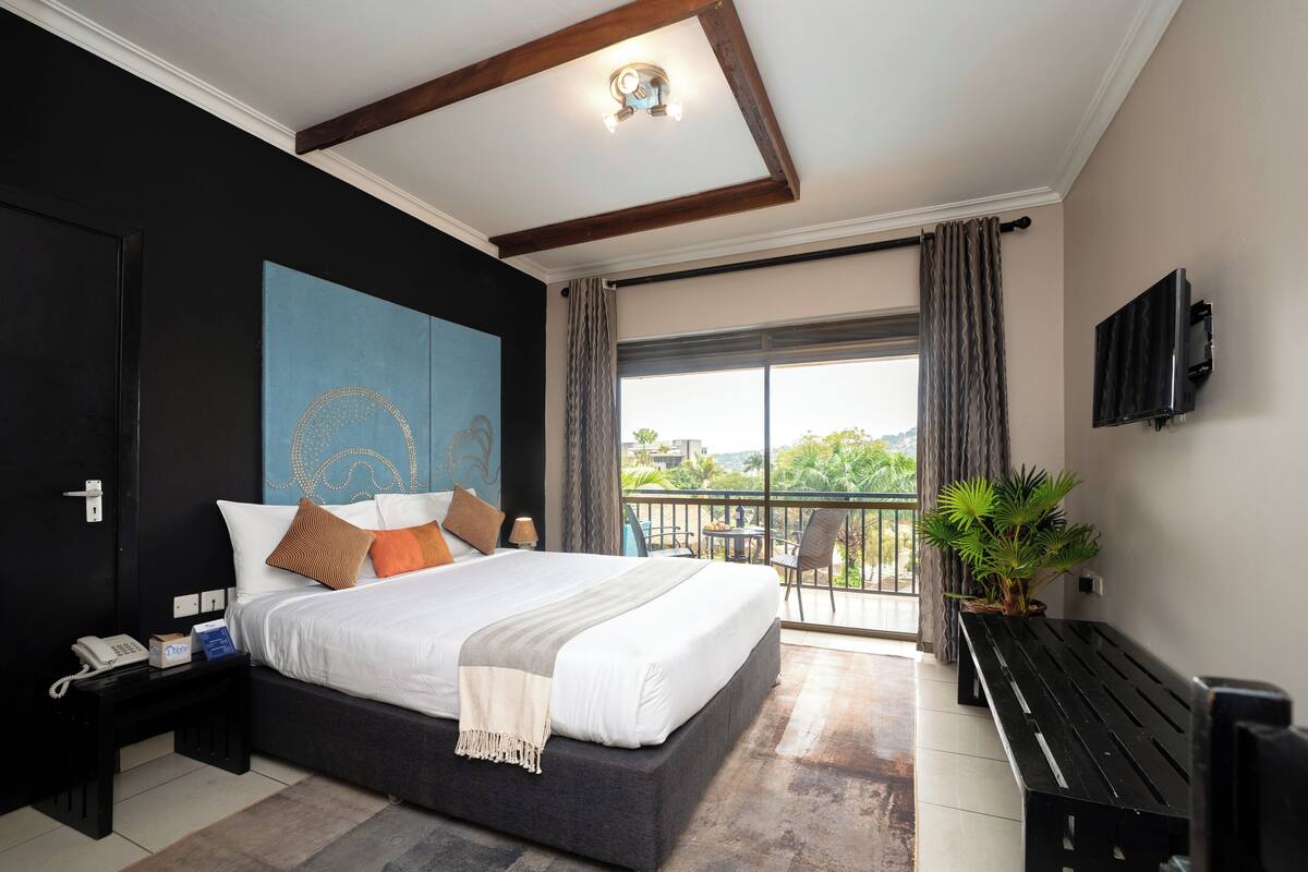 Une chambre d’hôtel moderne dotée d’un grand lit, d’un petit bureau, d’un balcon avec vue et d’un téléviseur fixé au mur.