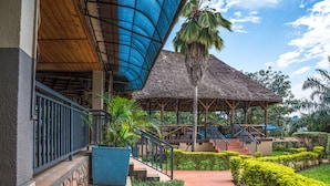 A covered outdoor area with a wooden ceiling, a thatched-roof structure, and a staircase leading to an upper level. - Dolphin Suites (Kampala)