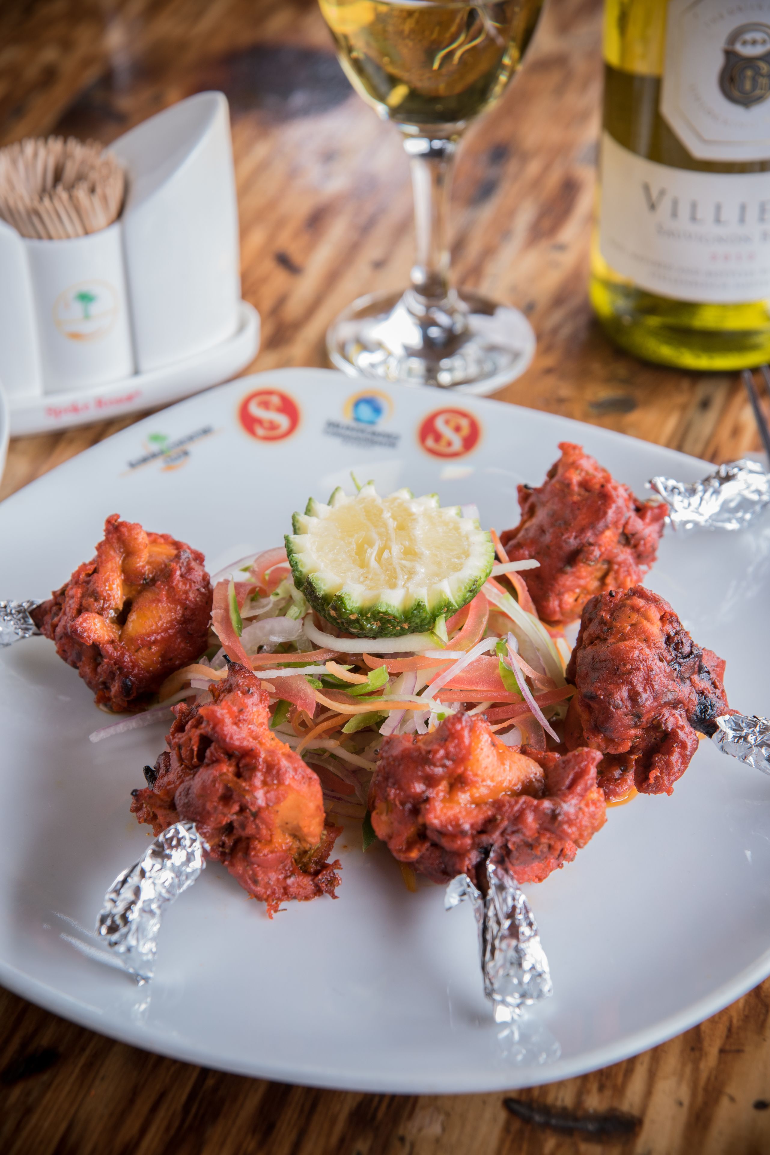 A plate of tandoori chicken skewers with a lime wedge and salad on a white plate.