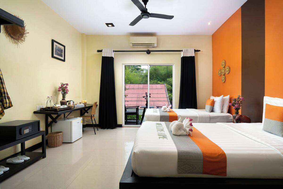 Habitación de hotel con dos camas, un escritorio, una silla, una mesita y un ventilador de techo.