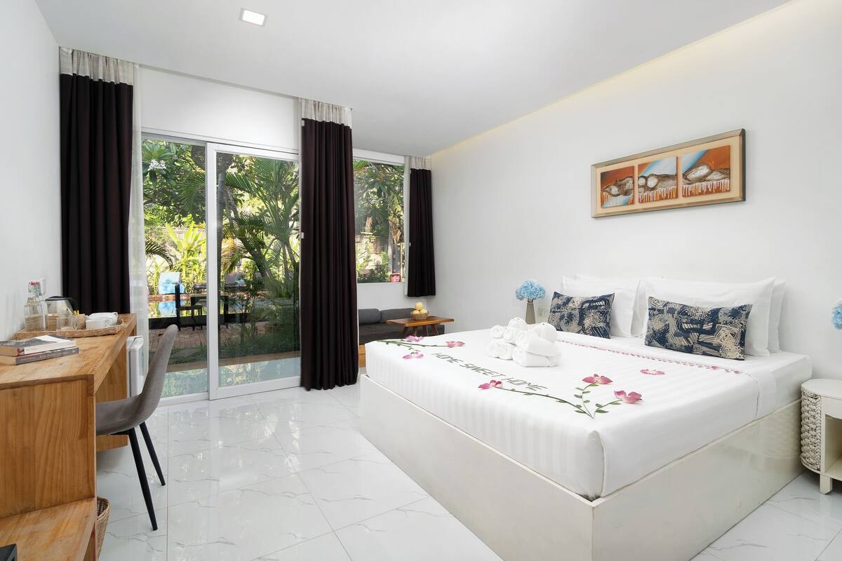 Habitación de hotel con cama, escritorio, silla, una mesita y vista a zonas verdes.