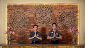 Two receptionists standing in front of a brick wall with three large woven wall hangings. - Home Indochine D'angkor (Siem Reap)