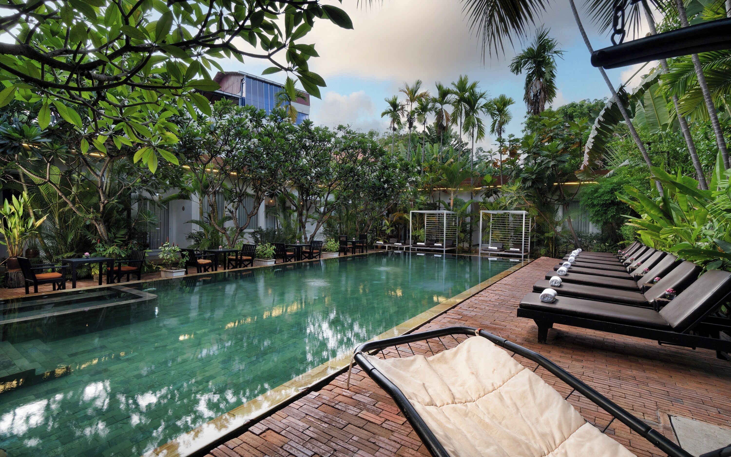 A poolside area with lounge chairs, a seating area with tables, and lush greenery.