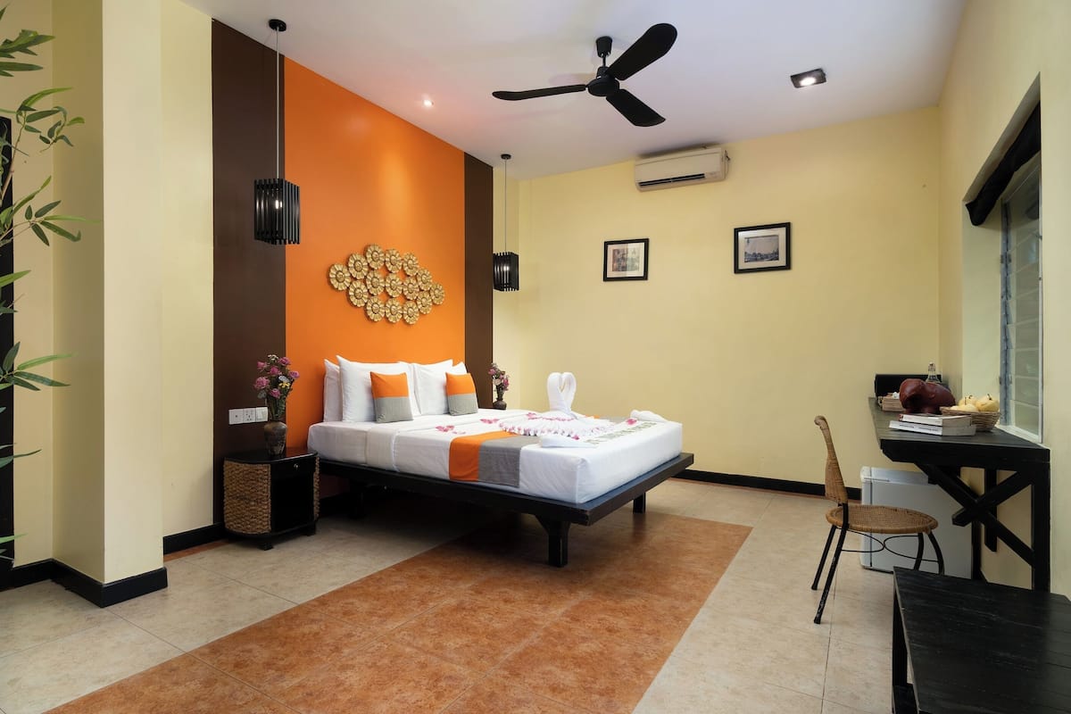 Una habitación de hotel con una cama, un escritorio, una silla, un ventilador de techo y un equipo de aire acondicionado.
