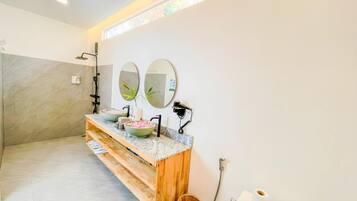 A modern bathroom with two sinks, a large mirror, and a shower area.