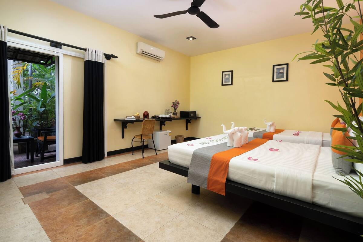 Habitación de hotel con cama, escritorio, silla, un refrigerador pequeño y puerta corrediza a un balcón.