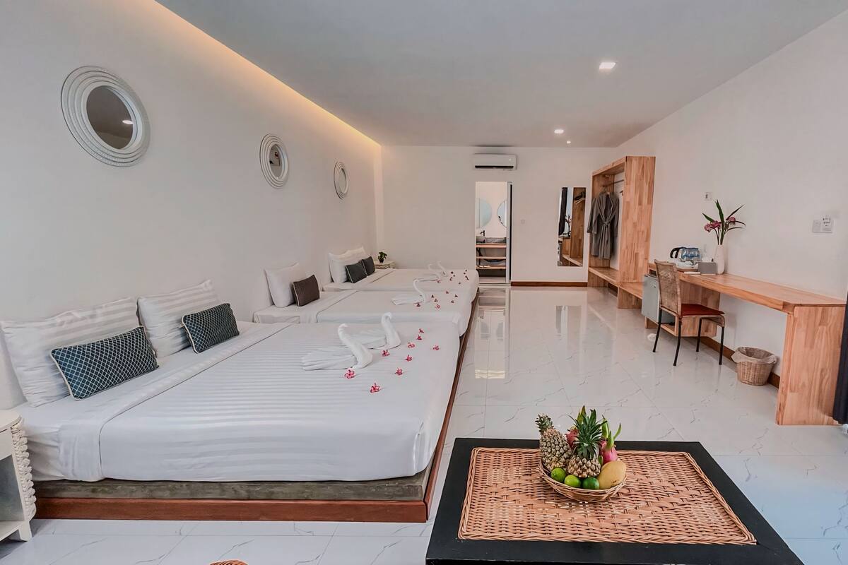 Habitación de hotel con una cama grande, un escritorio, una silla, una pequeña mesa con fruta y un espejo en la pared.