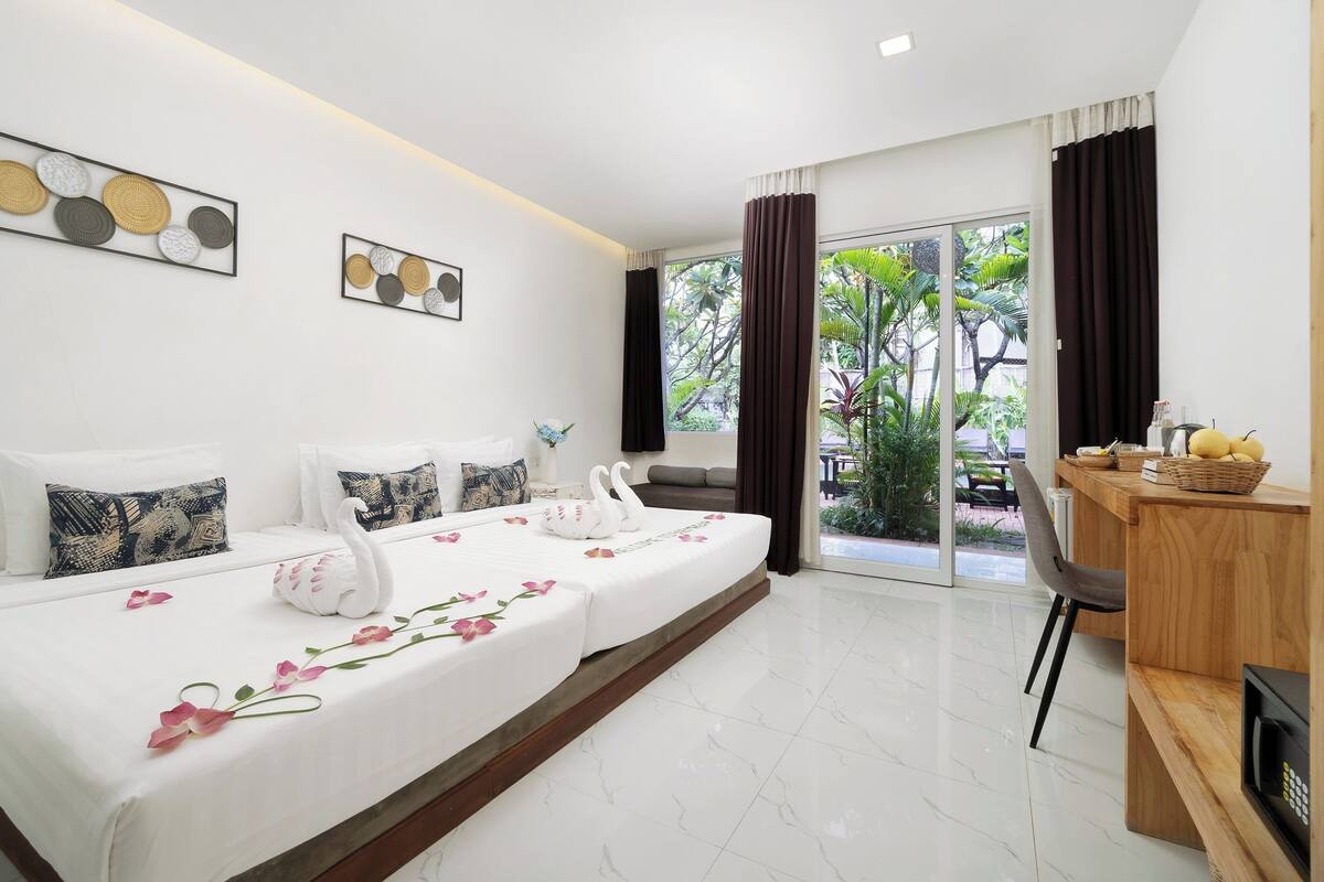 Habitación de hotel con una cama grande, un escritorio con una cesta y vistas al exterior con vegetación.