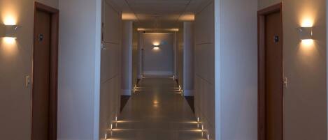 A long, narrow hallway with doors on both sides, illuminated by wall-mounted lights.