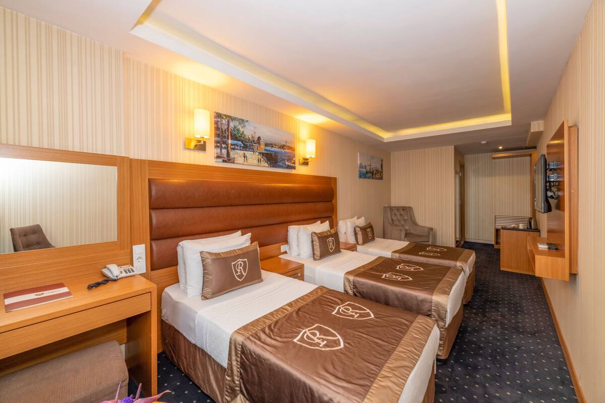 Ein Hotelzimmer mit drei Betten, einem Schreibtisch, einem Sessel und einem Fernseher.