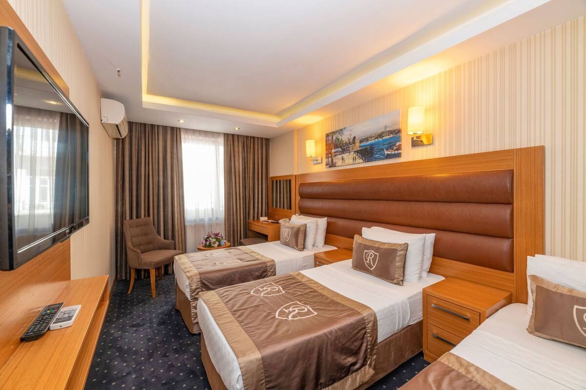 Ein Hotelzimmer mit zwei Betten, einem Schreibtisch, einem Fernseher und einem Bild an der Wand.