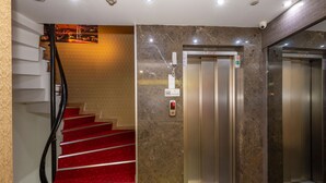 A hotel lobby with a marble wall, a red carpeted staircase, and an elevator. - Regno Hotel (Istanbul)