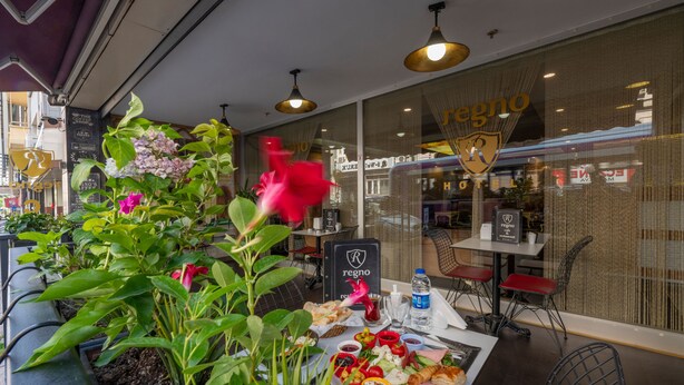 An outdoor dining area with a table set for a meal, surrounded by potted plants and a view of a restaurant named 'regno'. - Regno Hotel (Istanbul)
