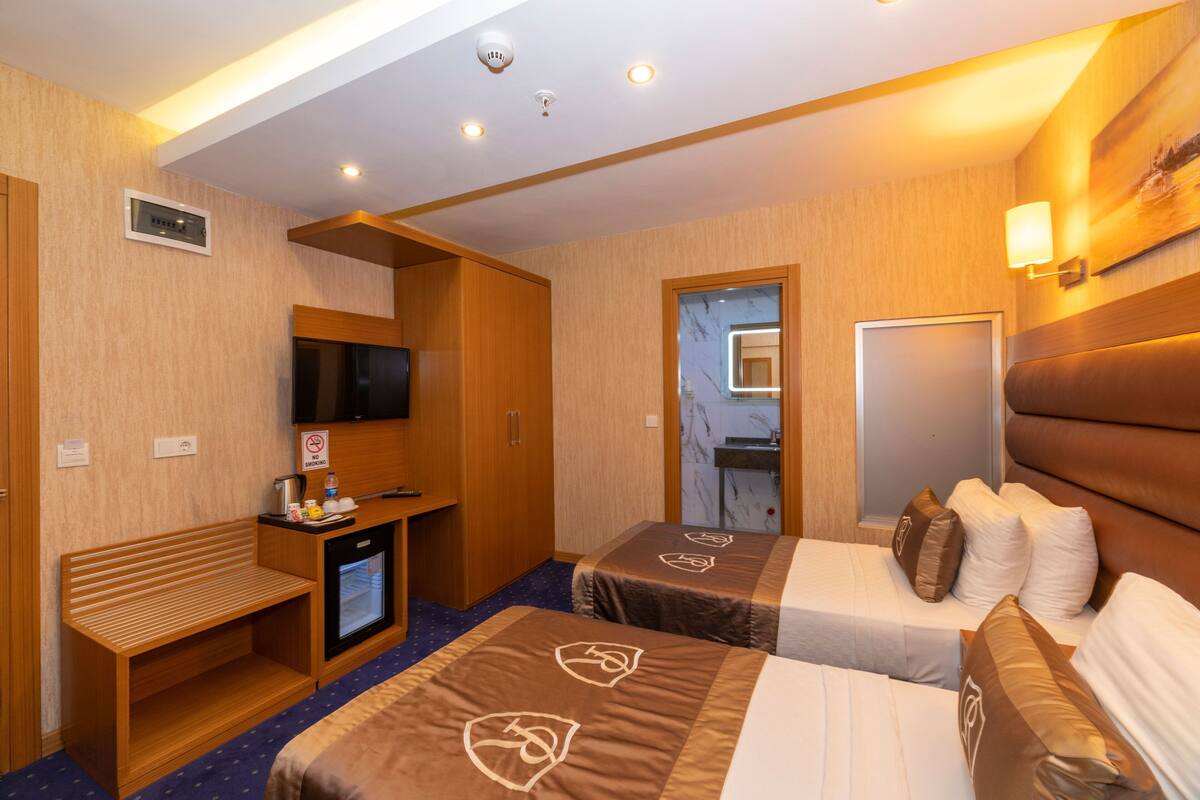 Ein Hotelzimmer mit zwei Betten, einem Schreibtisch, einem Fernseher, einer Minibar und einem Spiegel im Badezimmer.