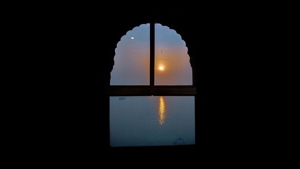A window with a reflection of the sun and a silhouette of a boat. - Palace on steps (Varanasi)